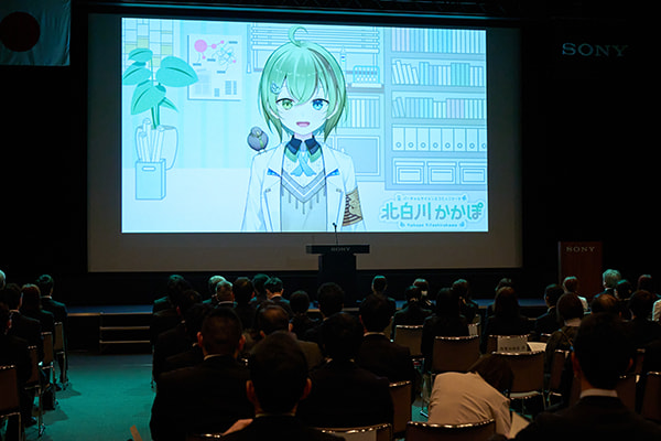 スクリーンに司会のかかぽさんがうつっている