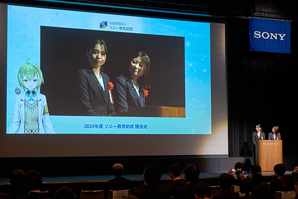 右手の演題に最優秀園 加納幼稚園の2名の先生、スクリーンには先生方とかかぽさんのやりとりが映し出されている