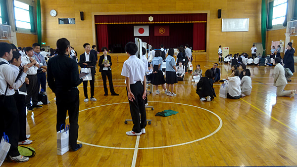 体育館で児童生徒たちが複数のグループに分かれてポスターを使い発表している。その周囲で参加者が発表を聞いている