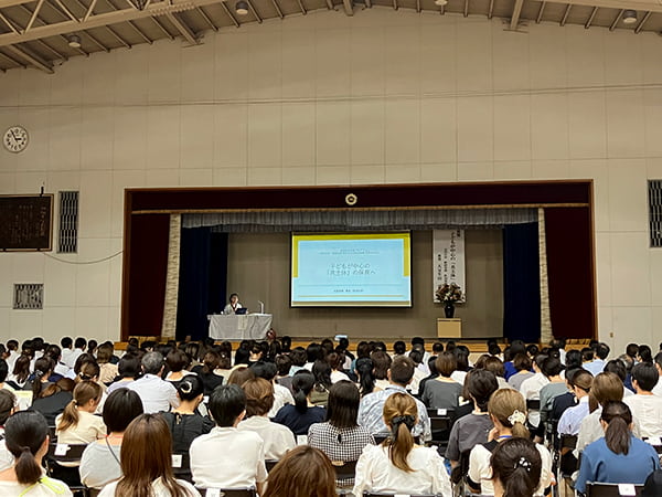 加納小学校の体育館で、大豆生田先生の講話を聴く参加者たち