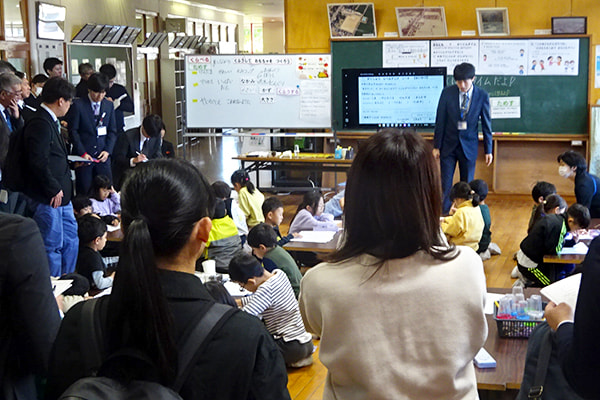 子どもたちが授業のまとめをノートに書いているところを参観する参加者
