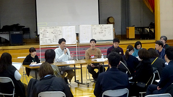 長机に座る研究会メンバーと向かい合って座っている大勢の参加者が対話している様子