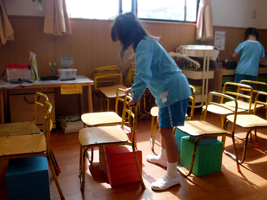 床に並べた木製の椅子のしたにソフト積木を入れている子どもの様子