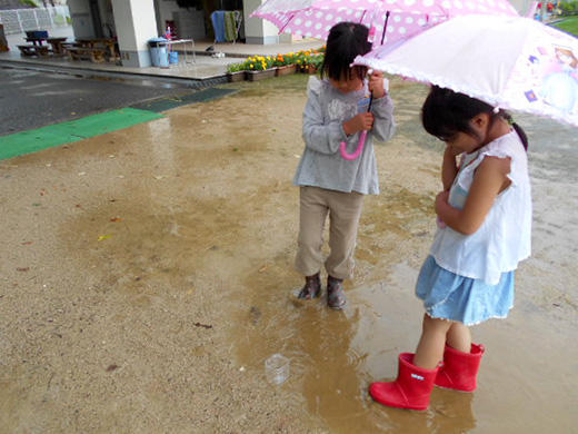 傘をさしながら水たまりに足を入れている子どもたちの写真